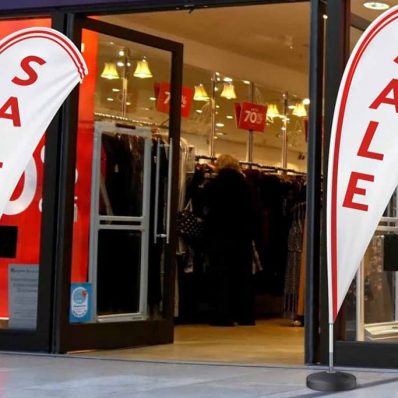 Sale sign displayed in front of clothing store, featuring For Sale teardrop flying banner on wrap around hem and tank base