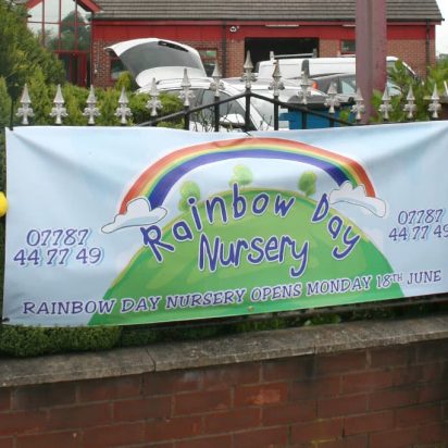 A digitally printed PVC banner displaying a rainbow, hanging on a fence at Rainbow Day Nursery