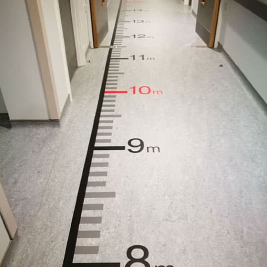 Hospital floor interior wayfinding graphics banner Interior of hospital corridor featuring ruler on floor for wayfinding assistance